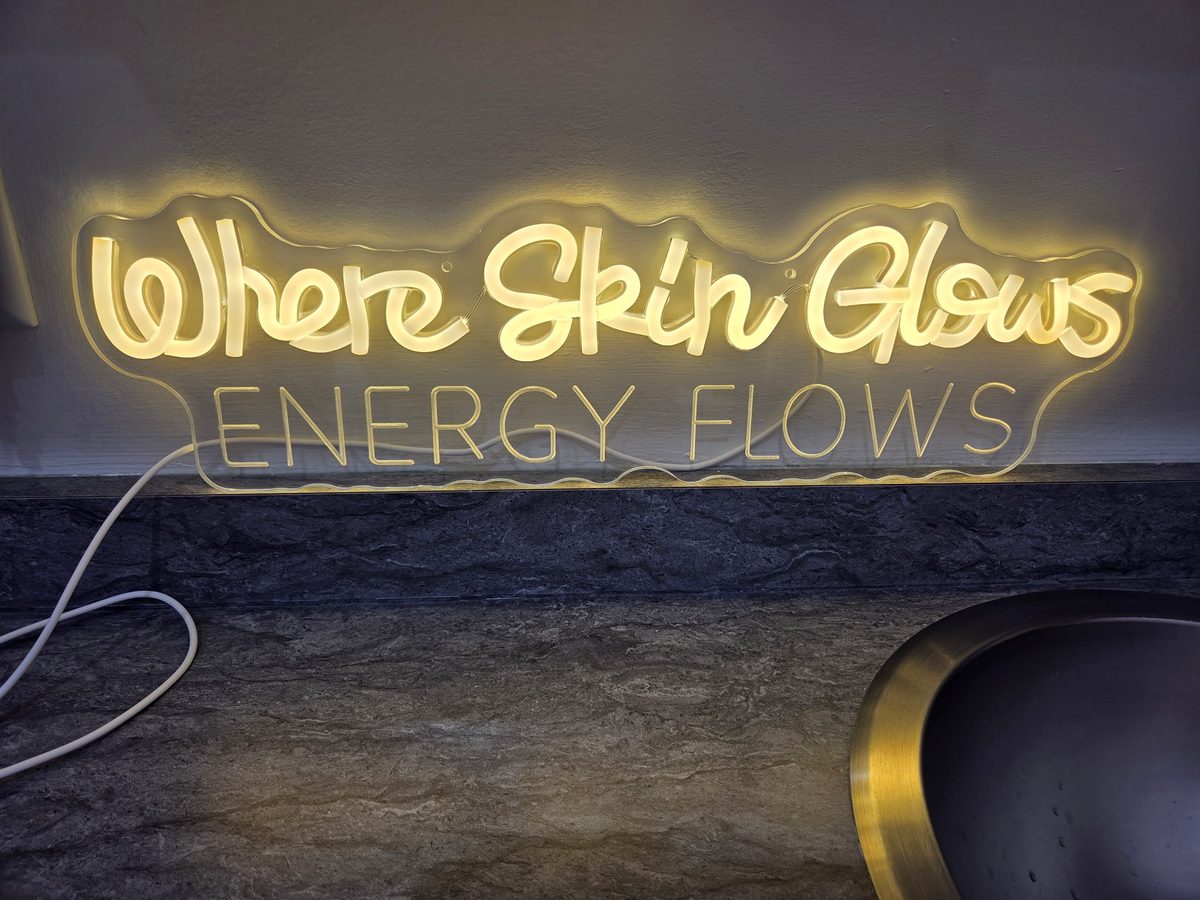 Where Skin Glows, Energy Flows neon sign above the studio sink